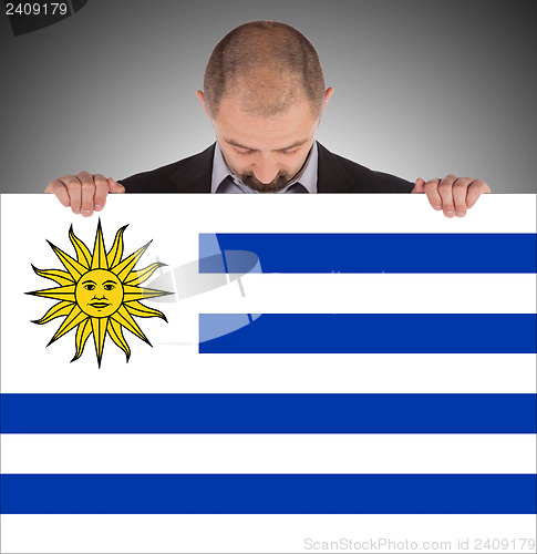 Image of Smiling businessman holding a big card, flag of Uruguay