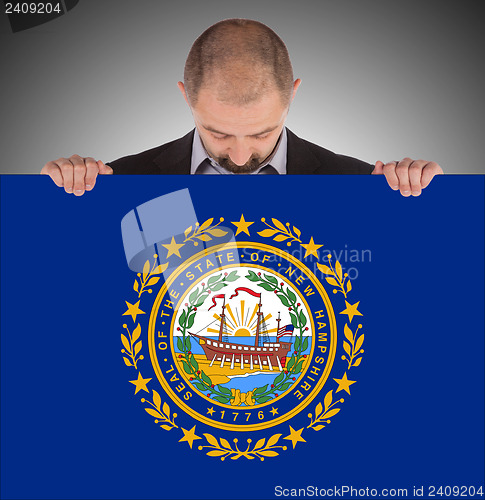 Image of Smiling businessman holding a big card, flag of New Hampshire