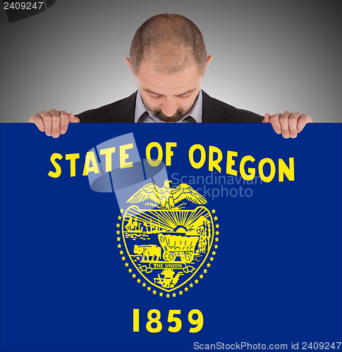 Image of Smiling businessman holding a big card, flag of Oregon