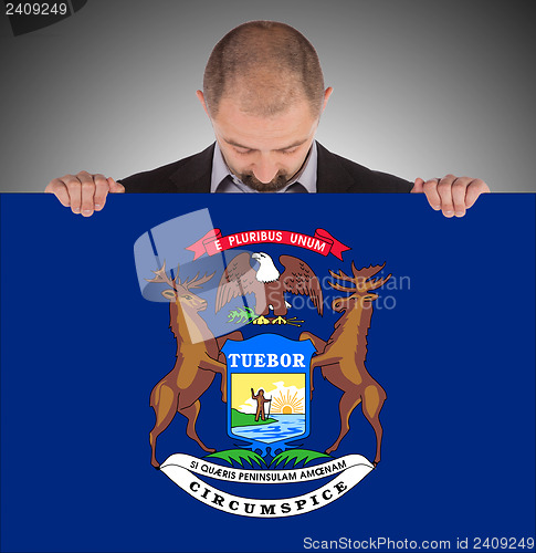 Image of Smiling businessman holding a big card, flag of Michigan