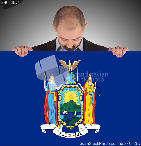 Image of Smiling businessman holding a big card, flag of New York