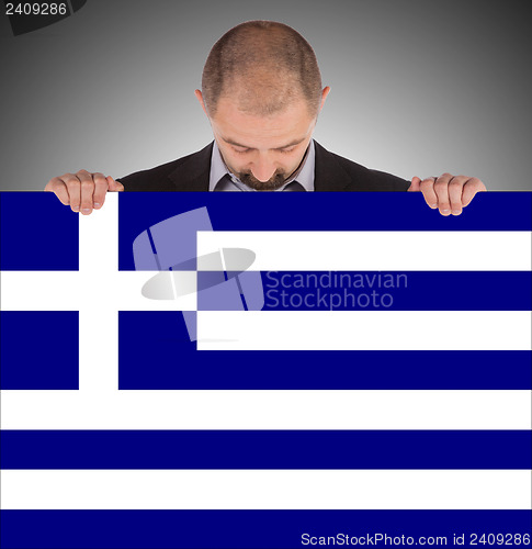 Image of Smiling businessman holding a big card, flag of Greece