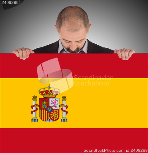 Image of Smiling businessman holding a big card, flag of Spain