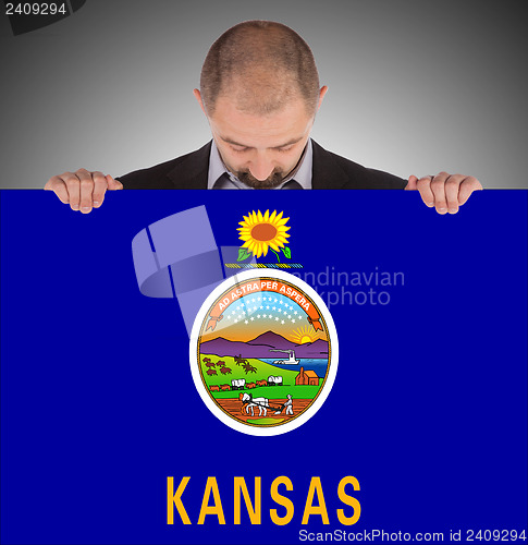 Image of Smiling businessman holding a big card, flag of Kansas