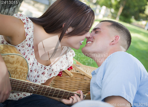 Image of Mixed Race Couple with Guitar Kissing in the Park