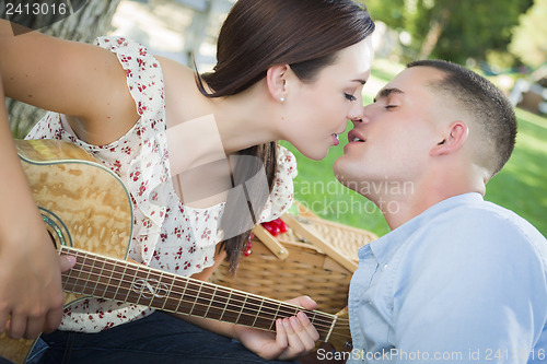Image of Mixed Race Couple with Guitar Kissing in the Park