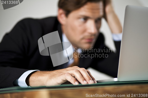 Image of Businessman rests his head in one hand while working on laptop