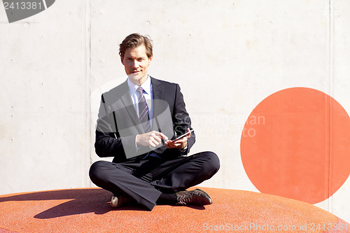 Image of Businessman sitting cross-legged using tablet