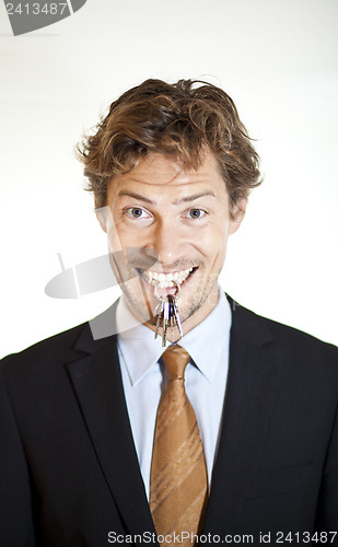 Image of Smiling businessman holding keys between his teeth