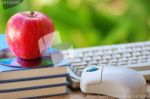 Image of Red apple on book, DVD and mouse