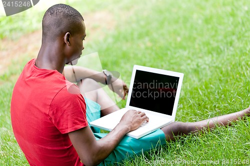 Image of young smiling african student sitting in grass with notebook