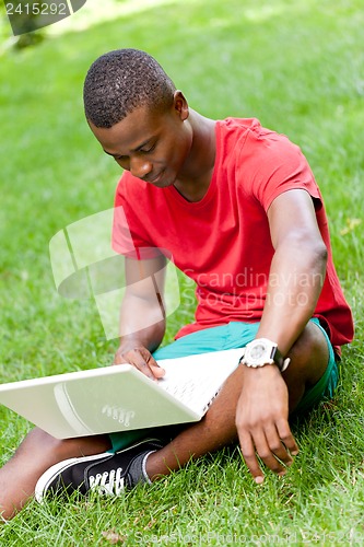 Image of young smiling african student sitting in grass with notebook