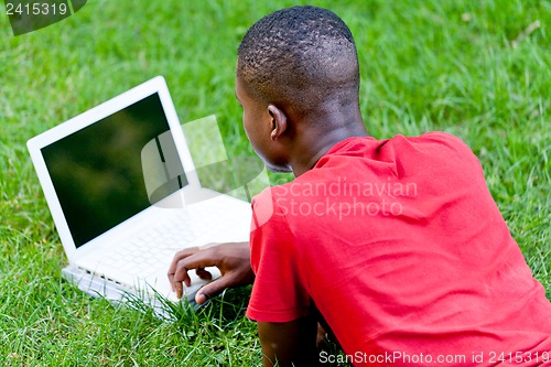 Image of young smiling african student sitting in grass with notebook