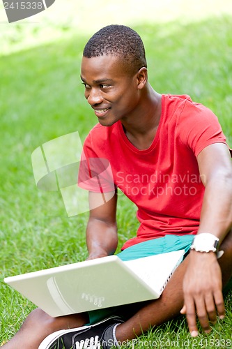 Image of young smiling african student sitting in grass with notebook