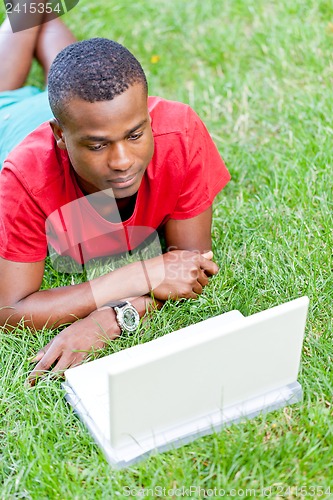 Image of young smiling african student sitting in grass with notebook