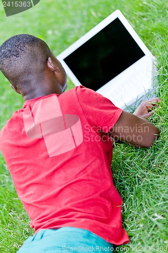 Image of young smiling african student sitting in grass with notebook