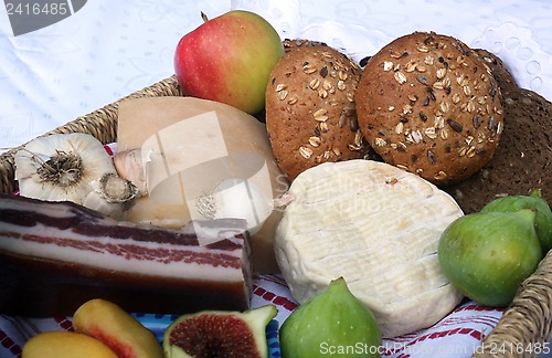 Image of Rustic still life of bread, cheese, bacon and figs in a wicker basket