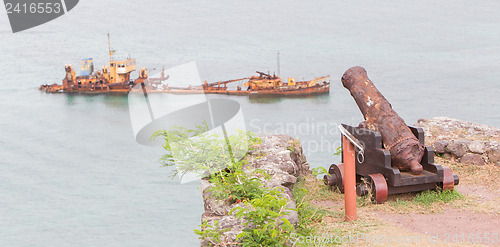 Image of Old rusted canon pointing at a sunken ship, concept of humor