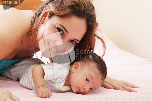 Image of Hispanic mom lying down on bed and holding her infant son