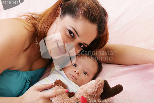 Image of Happy mum and baby boy smiling in the bed holding teddy bear