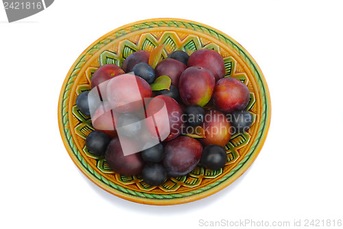 Image of Ripe plums and prunes on ceramic dish on a white background.