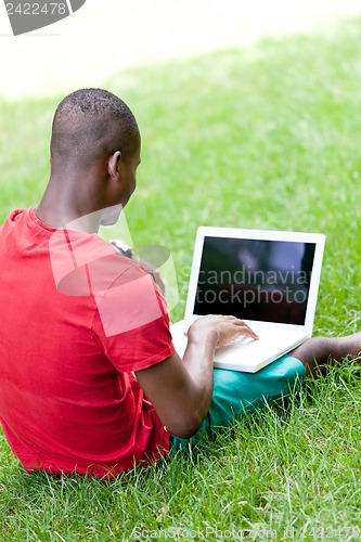 Image of young smiling african student sitting in grass with notebook