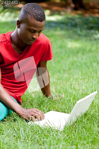 Image of young smiling african student sitting in grass with notebook