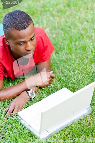 Image of young smiling african student sitting in grass with notebook