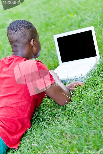 Image of young smiling african student sitting in grass with notebook