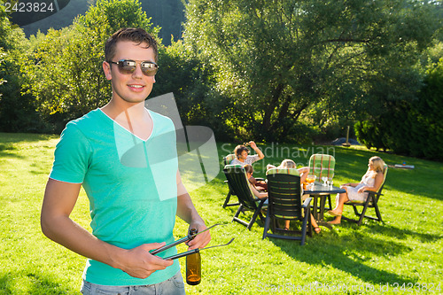 Image of Man Holding Tongs And Wine Bottle At Garden Party