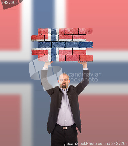 Image of Businessman holding a large piece of a brick wall