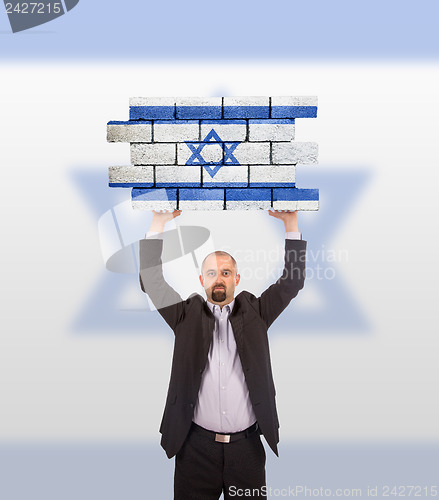 Image of Businessman holding a large piece of a brick wall