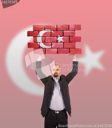 Image of Businessman holding a large piece of a brick wall