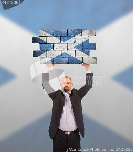 Image of Businessman holding a large piece of a brick wall