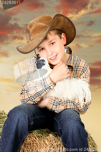 Image of Farm boy sitting on bale of hay holding a chicken