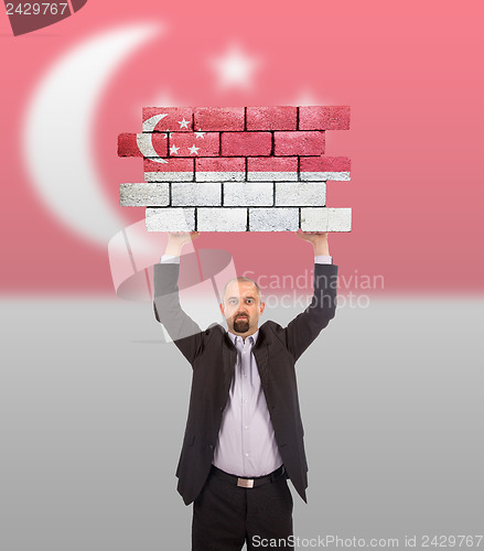 Image of Businessman holding a large piece of a brick wall