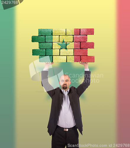 Image of Businessman holding a large piece of a brick wall