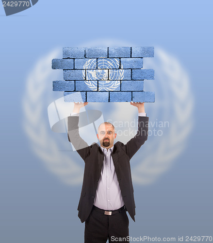 Image of Businessman holding a large piece of a brick wall