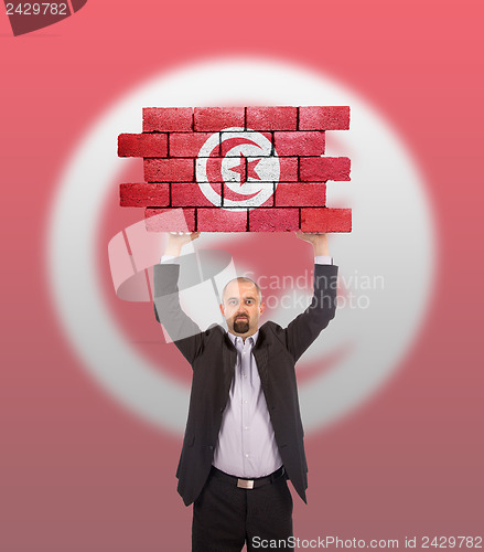 Image of Businessman holding a large piece of a brick wall