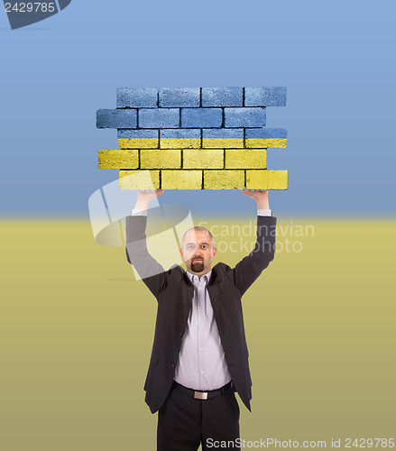 Image of Businessman holding a large piece of a brick wall