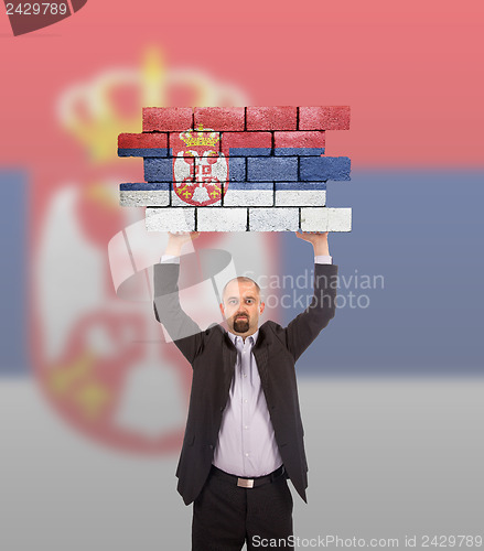 Image of Businessman holding a large piece of a brick wall