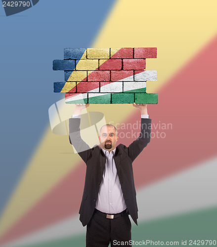 Image of Businessman holding a large piece of a brick wall