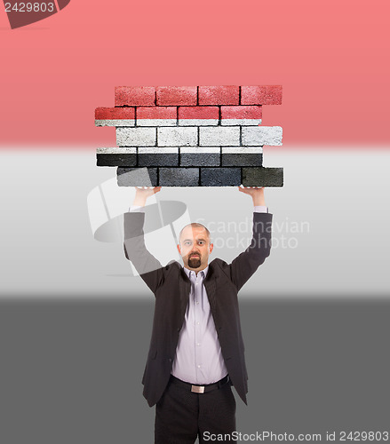 Image of Businessman holding a large piece of a brick wall