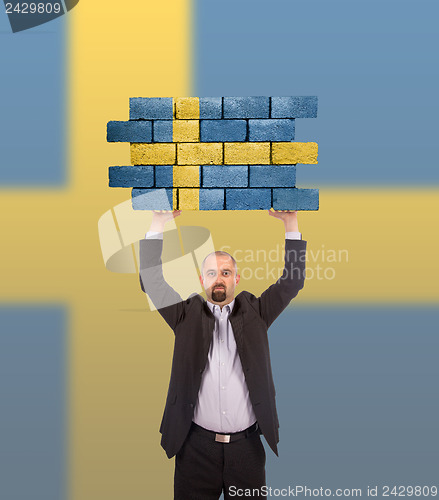 Image of Businessman holding a large piece of a brick wall