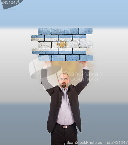 Image of Businessman holding a large piece of a brick wall