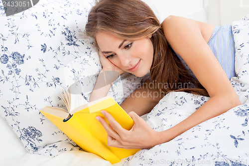 Image of young attractive woman reading book lying in bed