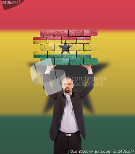 Image of Businessman holding a large piece of a brick wall