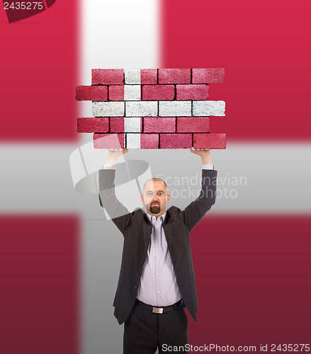 Image of Businessman holding a large piece of a brick wall