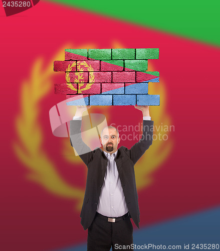 Image of Businessman holding a large piece of a brick wall