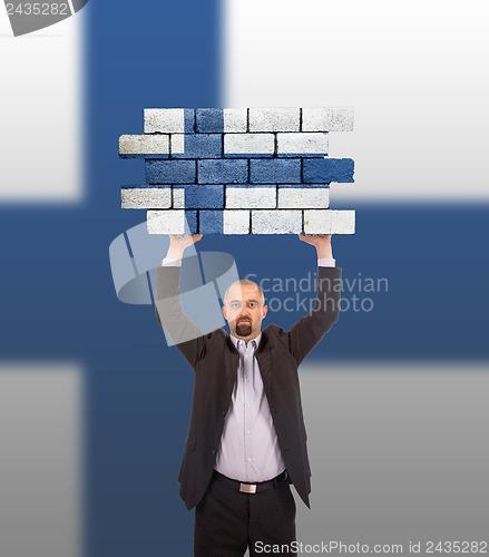 Image of Businessman holding a large piece of a brick wall